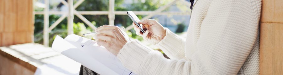 Smiling man with blueprint and mobile phone sitting on window sill at construction site