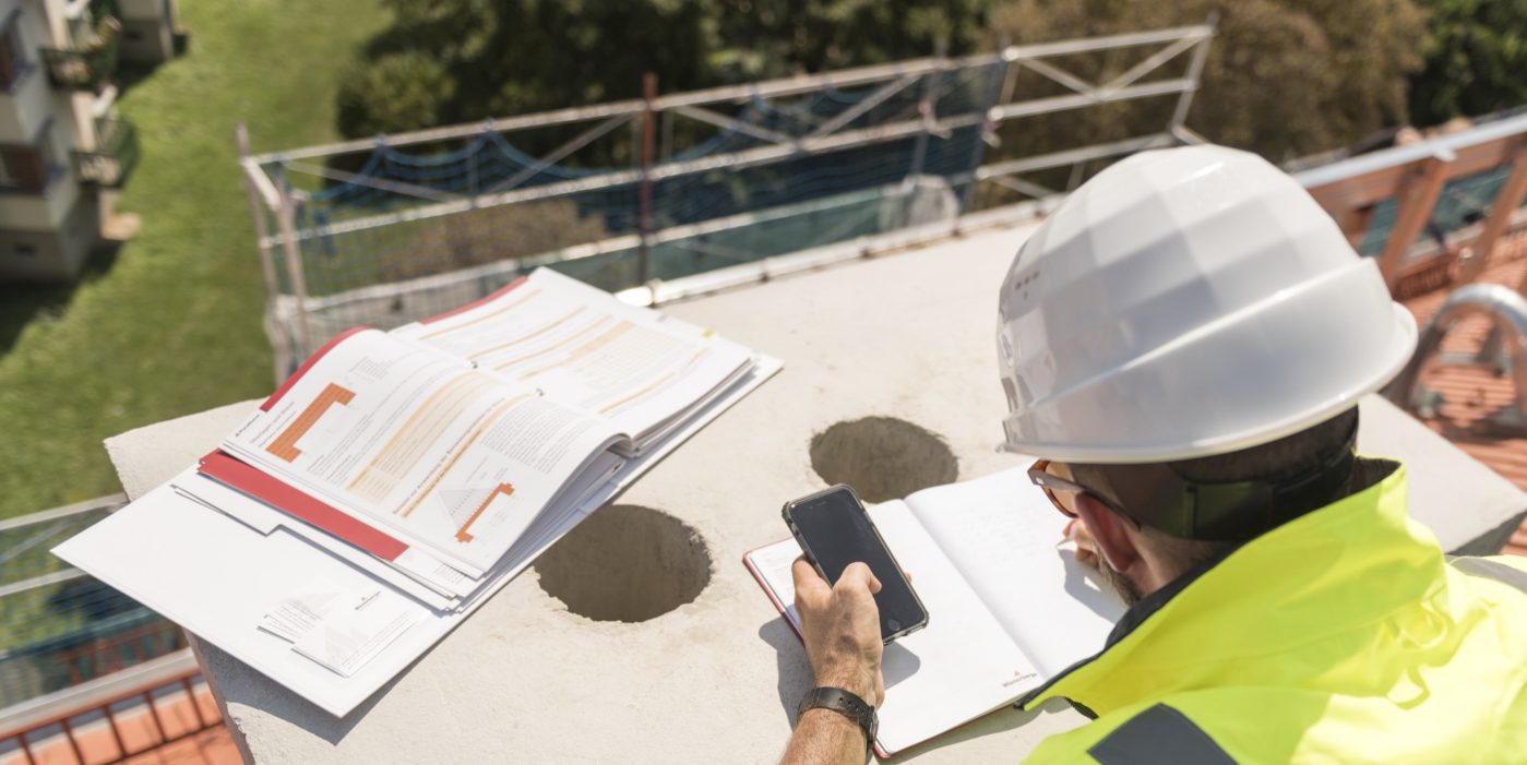Urban roofer taking notes holding iPhone and writing in an urban location wearing hard hat and safety jacket, Fast Forward Commercial Excellence